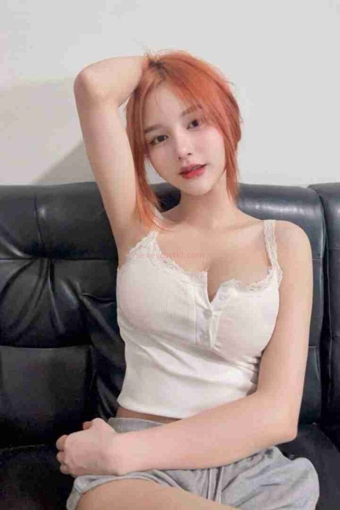 Attractive Asian woman with orange hair in white top on black sofa.