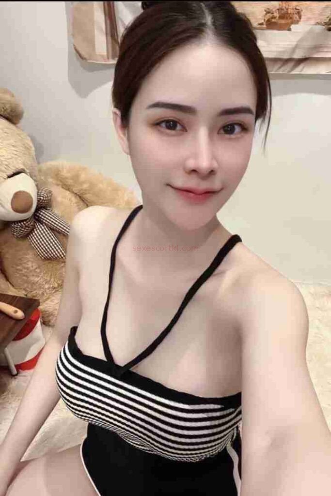 Attractive Asian woman in striped top, teddy bear in background. Mild Escort Girl Malaysia.