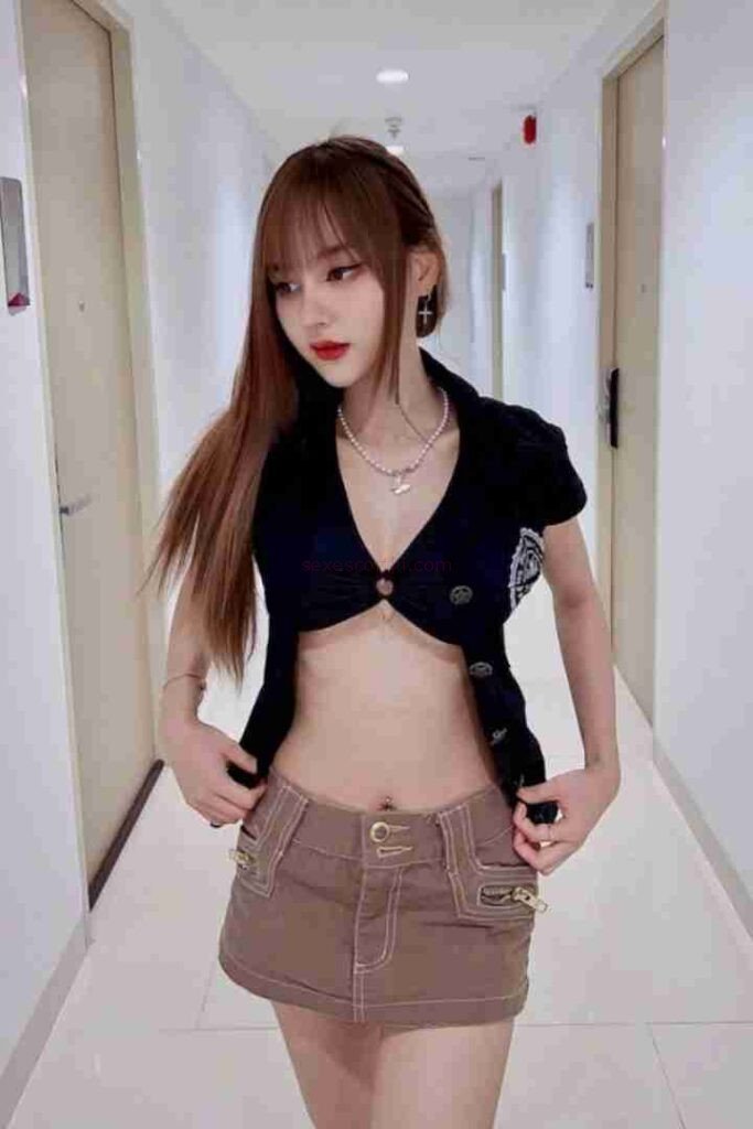 Kannika, a Thai escort, poses in a hallway. She wears a cropped top and mini skirt.