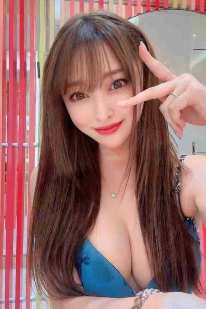 Attractive Asian woman (Li Jing) with long brown hair and red lipstick making a peace sign.