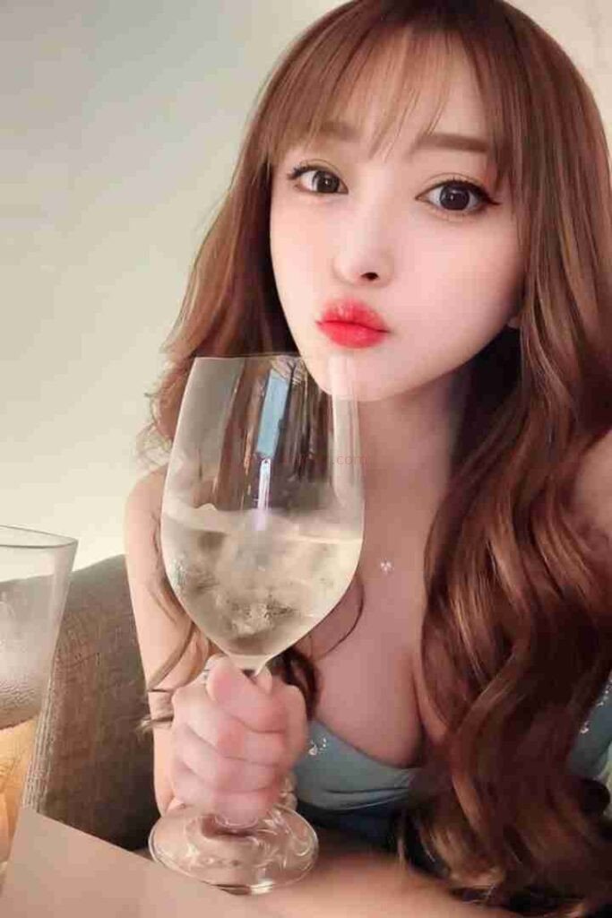 Li Jing, Chinese escort, holding a glass of white wine with red lipstick and long brown hair.