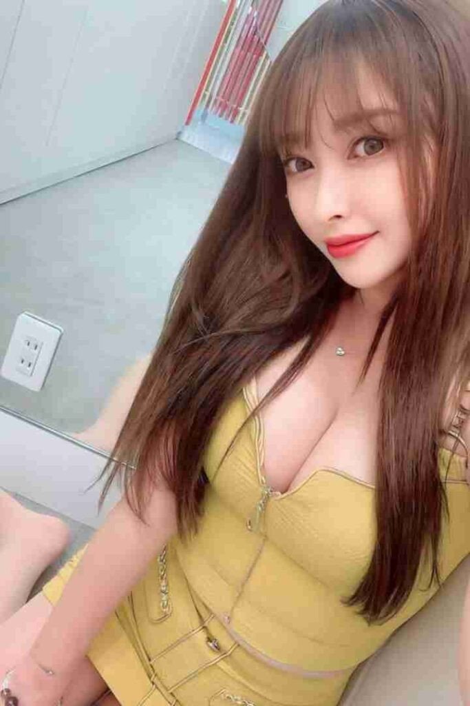 Li Jing, Chinese escort, in yellow dress with long brown hair and bangs, smiling at the camera.