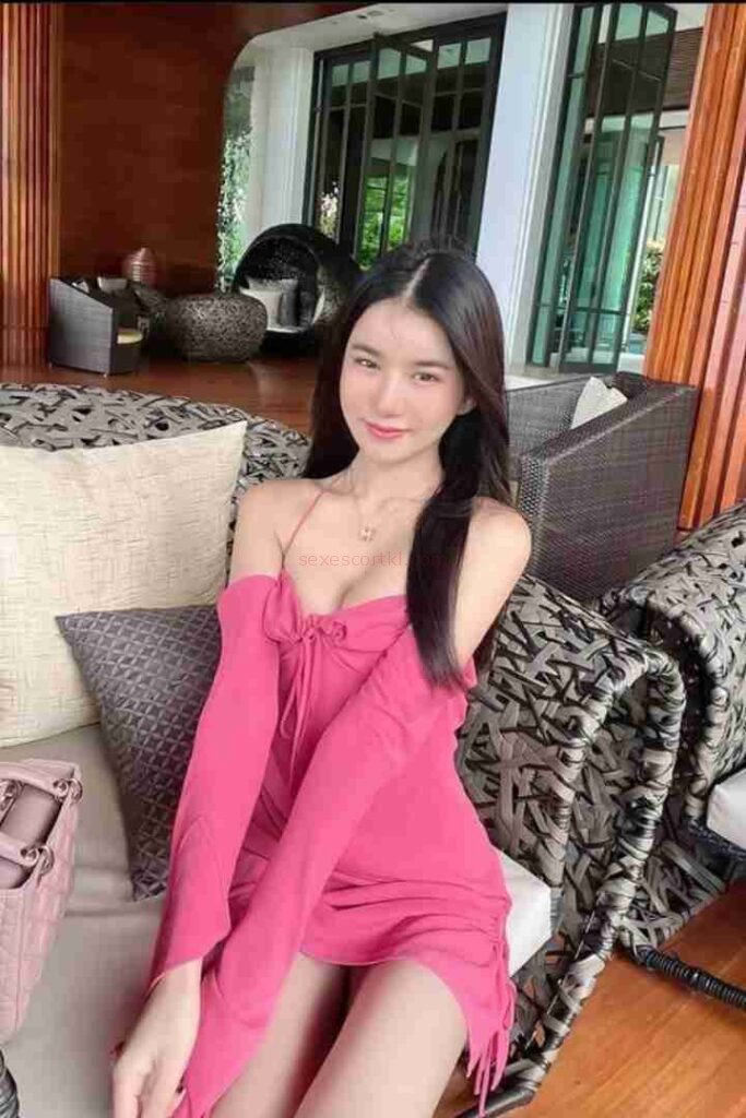 Ming Yue, Chinese call girl in pink dress, sitting on a sofa in a luxurious setting.