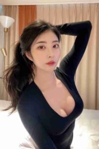 Attractive Asian woman in black top posing with arm up, dark hair in ponytail, light makeup.