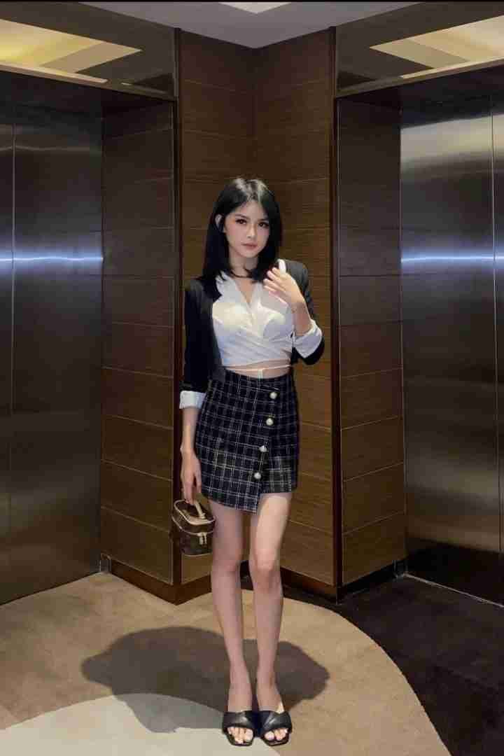 Woman in black blazer, white top, and plaid skirt stands in front of elevators.