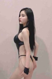 Woman in black lingerie with chain and handcuffs posing against a plain wall.