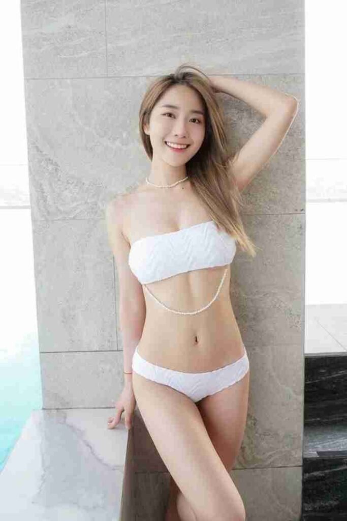 Smiling woman in white bikini with pearl necklace posing by poolside. Summer swimwear fashion.