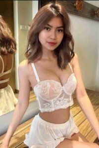 Woman in white lace lingerie top and shorts smiling, posing indoors with mirror reflection.
