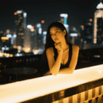 Woman at rooftop bar with city lights at night.