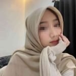 Sex Escort KL Girl Young woman in a beige hijab and sweater, resting her chin on her hand. Incall & Outcall Escorts Girl Service