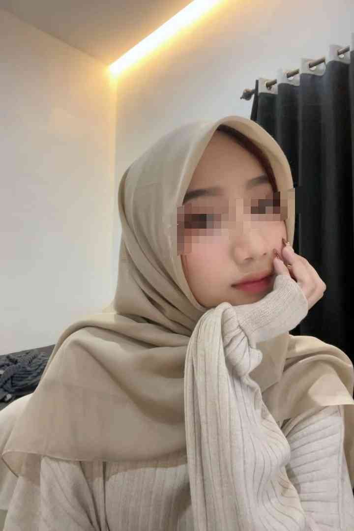 Sex Escort KL Girl Young woman in a beige hijab and sweater, resting her chin on her hand. Incall & Outcall Escorts Girl Service