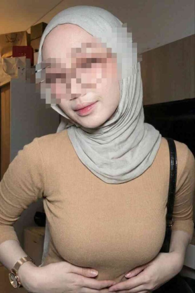 Sex Escort KL Girl Woman wearing a hijab and beige top, standing with hands on stomach Incall & Outcall Escorts Girl Service